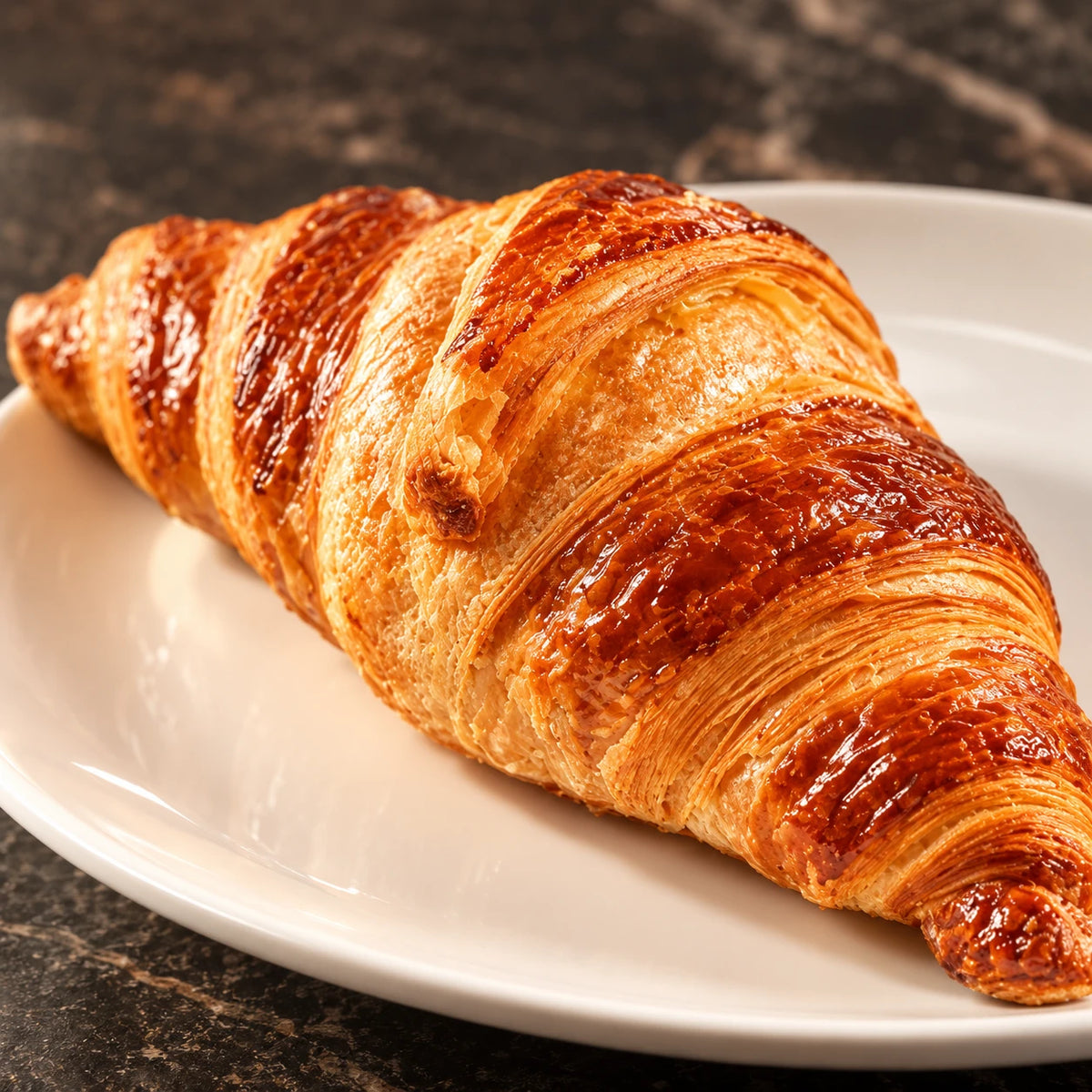 Primo piano degli strati sfogliati di un croissant al burro su un piatto bianco