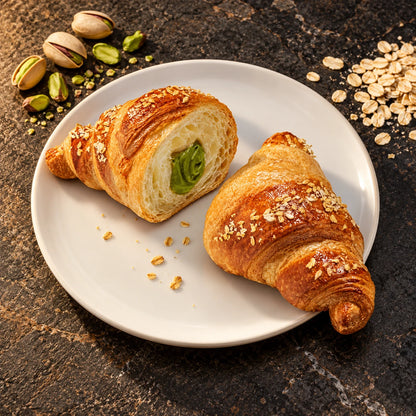 Pistachecroissant opengesneden met groene pistachecrème op een wit bord van bovenaf op donkere steen, met ingrediënten ernaast