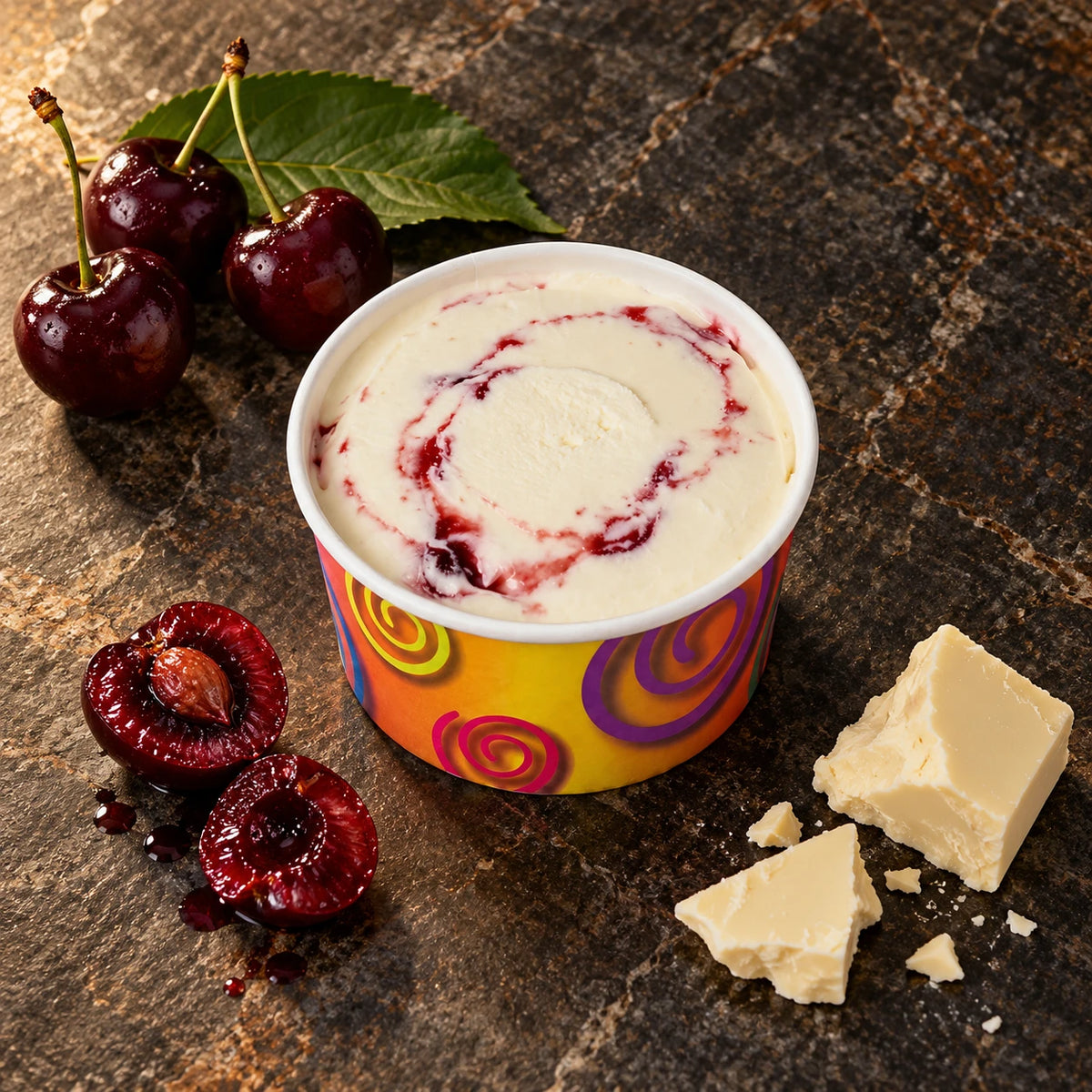 Vasito de helado de cereza amarena sobre piedra oscura, con cerezas frescas y una hoja