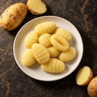 Plate of potato gnocchi from above on dark stone, fresh potatoes beside it