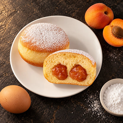 Krapfen all'Albicocca visto dall'alto su piatto bianco, con albicocche fresche, un uovo e una ciotola di zucchero a velo