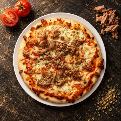 Pizza de atún vista desde arriba en un plato blanco sobre piedra oscura, junto a tomates, atún y orégano