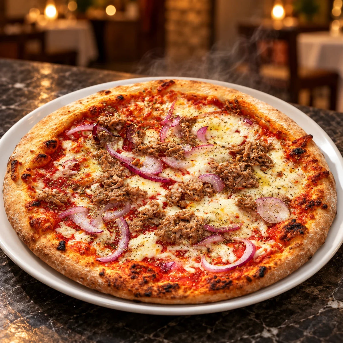 Parująca pizza z tuńczykiem i czerwoną cebulą na białym talerzu na stole w restauracji