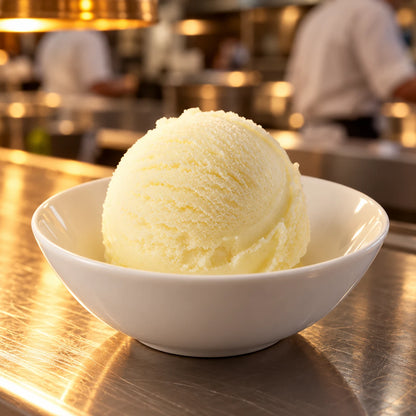 Cuenco blanco con una bola de sorbete de limón en el pase de una cocina profesional